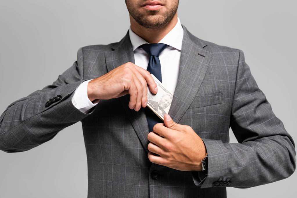 обрезанный вид бизнесмена в костюме, прячущего долларовые купюры, изолированные на сером
  - Фото, изображение