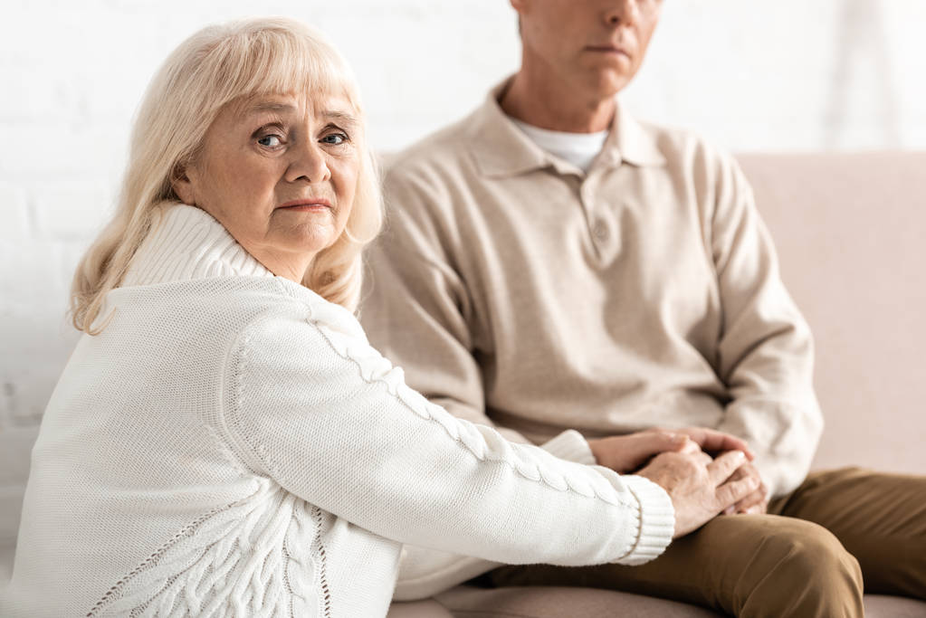 Selektiver Fokus einer traurigen Rentnerin, die ihrem Ehemann mit Alzheimer-Krankheit die Hand hält  - Foto, Bild