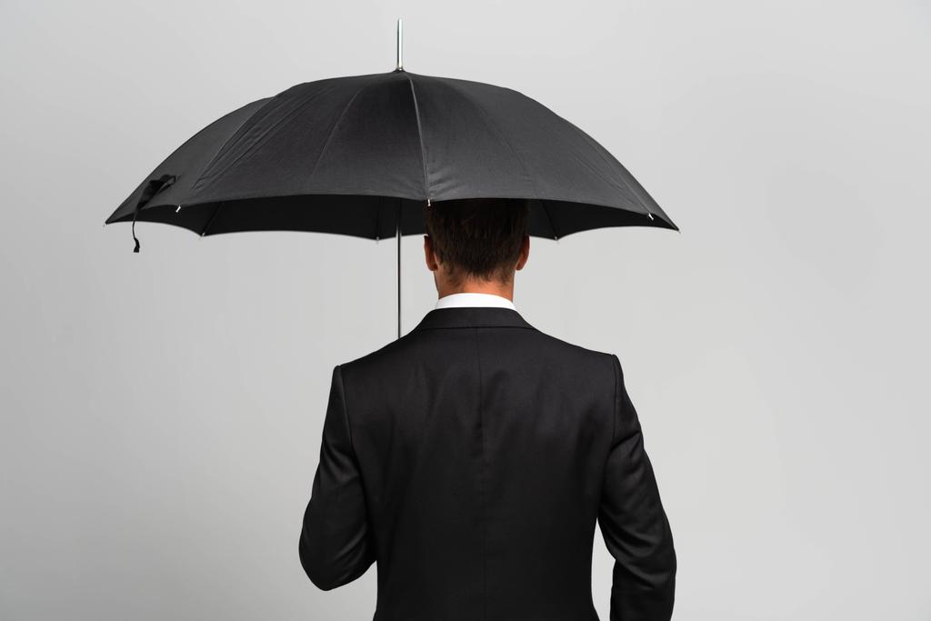 πίσω όψη του επιχειρηματία με κοστούμι κρατώντας ομπρέλα απομονωμένη σε γκρι  - Φωτογραφία, εικόνα