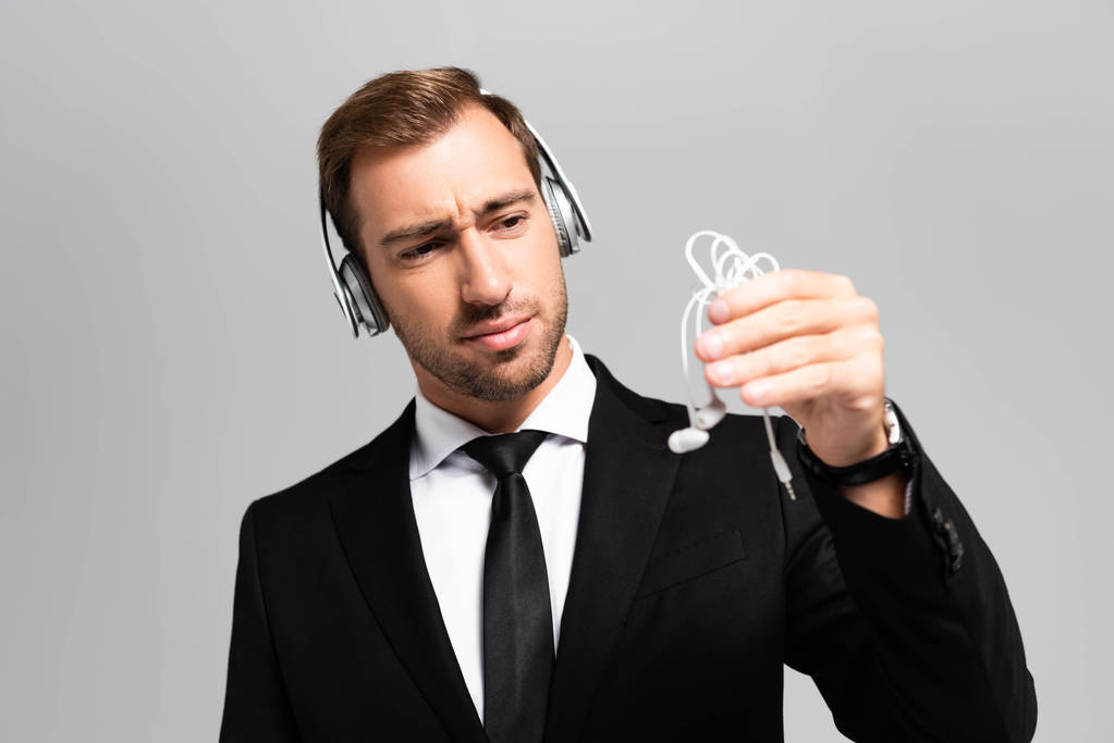 smutný podnikatel v obleku se sluchátky poslech hudby a při pohledu na sluchátka izolované na šedé  - Fotografie, Obrázek