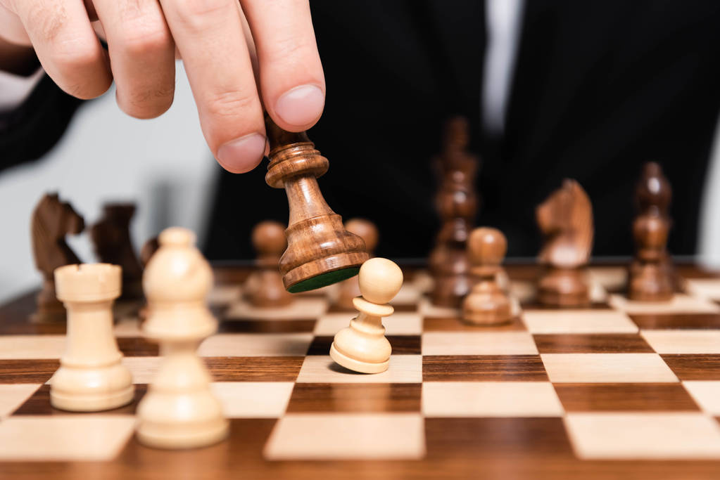 Ausgeschnittene Ansicht von Geschäftsmann, der Schachfigur über Schachbrett hält  - Foto, Bild