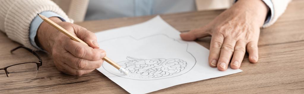panoramisch schot van gepensioneerde vrouw met papier met tekening op tafel  - Foto, afbeelding