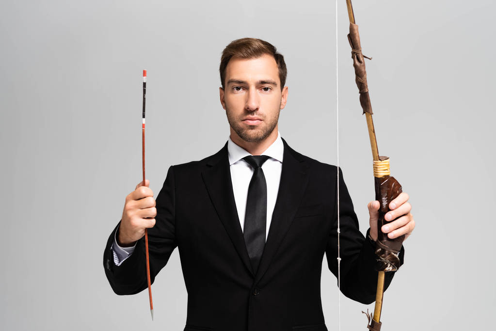 homem de negócios bonito em terno segurando arco e flecha isolado em cinza
  - Foto, Imagem