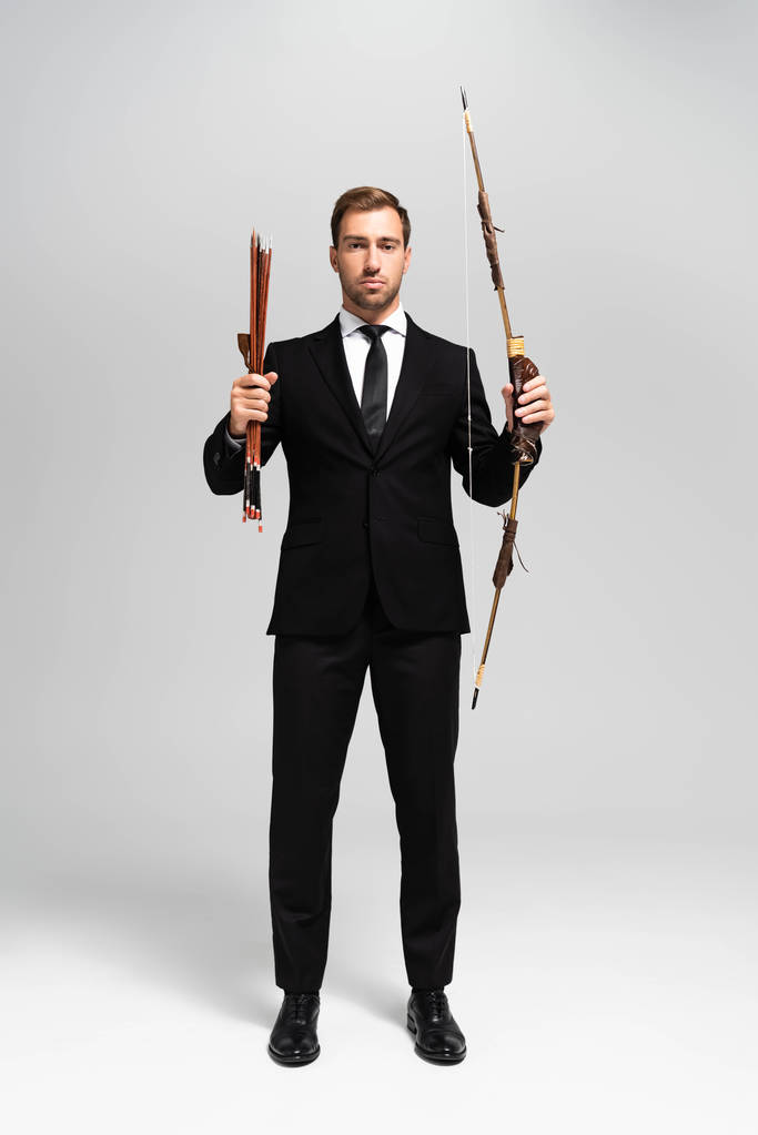 handsome businessman in suit holding bow and arrows on grey background  - 写真・画像