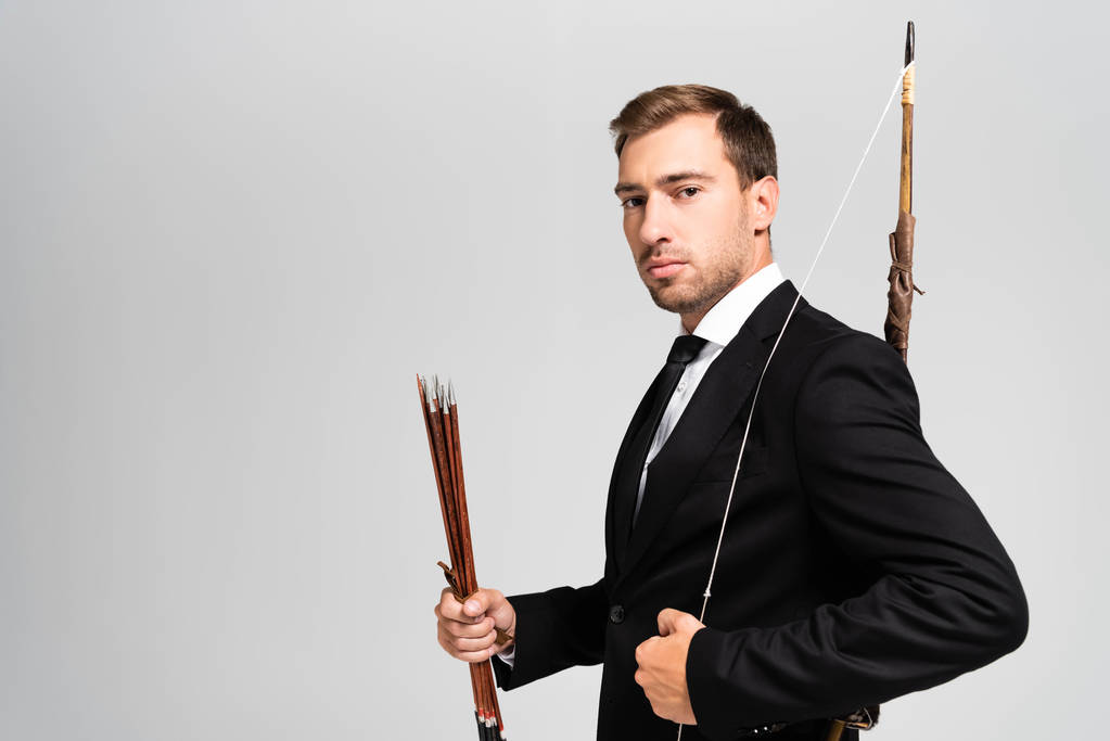 handsome businessman in suit holding bow and arrows isolated on grey  - 写真・画像