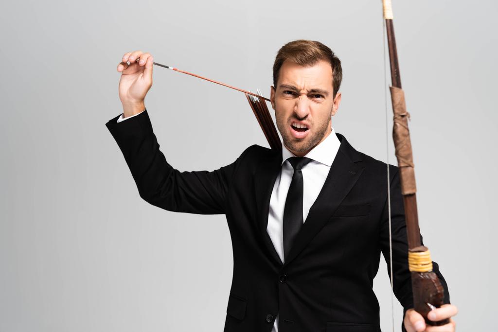 angry businessman in suit holding bow and arrow isolated on grey  - 写真・画像