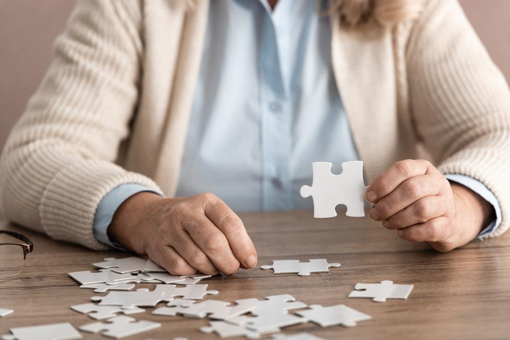 cropped view of retired woman with alzheimer holding puzzle piece - Photo, Image