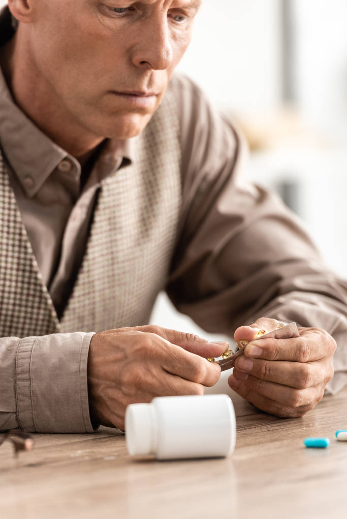 καλλιεργημένη άποψη του άρρωστου ηλικιωμένου άνδρα που κοιτάζει τα χάπια  - Φωτογραφία, εικόνα