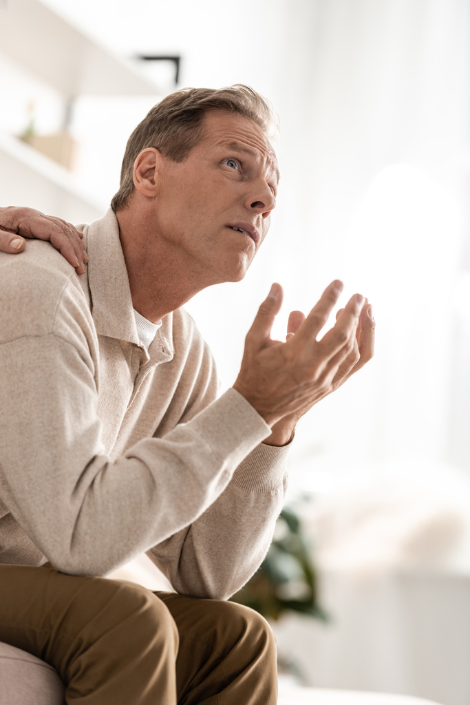 Ausgeschnittene Ansicht einer Seniorin, die die Schulter ihres kranken Mannes berührt, der zu Hause sitzt  - Foto, Bild