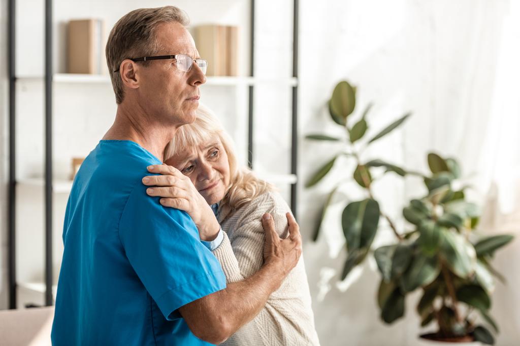 zdenerwowana seniorka z alzheimerem przytulająca się do lekarza w okularach  - Zdjęcie, obraz