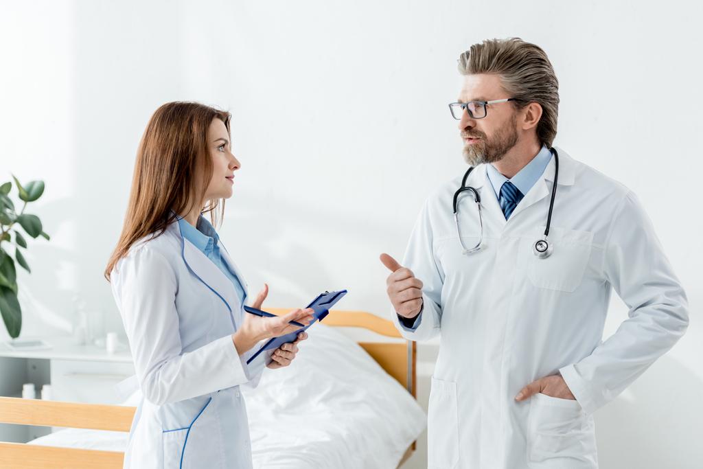 γιατρός με λευκό παλτό που δείχνει τον αντίχειρα προς τα πάνω και μιλάει με συνάδελφο στο νοσοκομείο  - Φωτογραφία, εικόνα