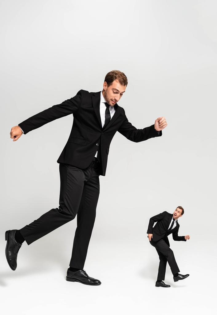 angry businessman in suit hitting frightened marionette on grey background  - Photo, Image