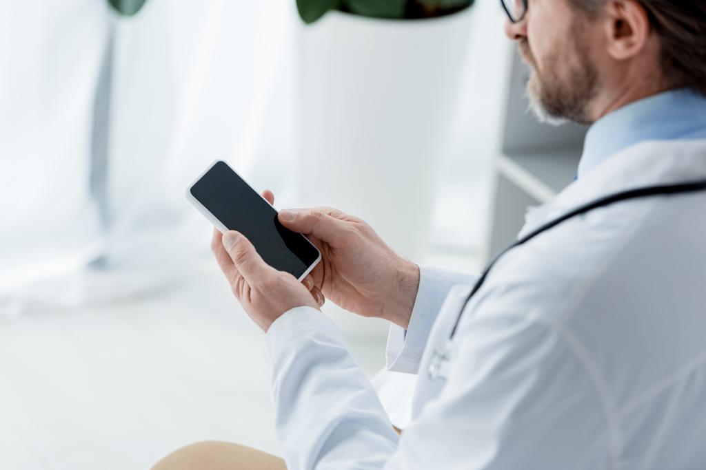 oříznutý pohled na lékaře v bílém plášti pomocí smartphonu v nemocnici  - Fotografie, Obrázek