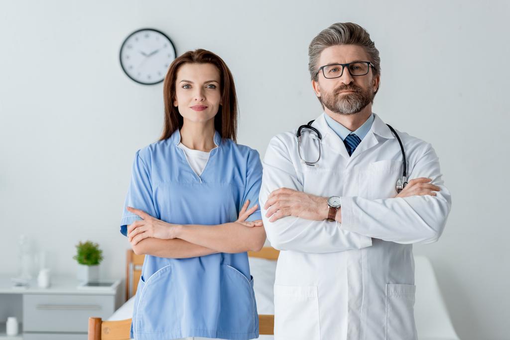 médecin en manteau blanc et infirmière attrayante avec les bras croisés regardant caméra à l'hôpital
  - Photo, image