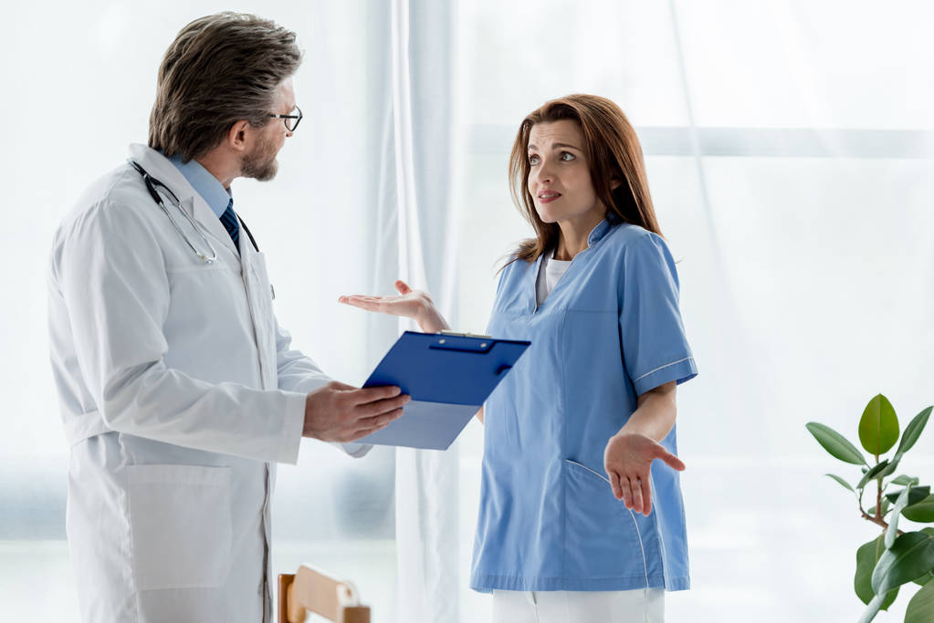 médico de casaco branco conversando com enfermeira chocada no hospital
   - Foto, Imagem