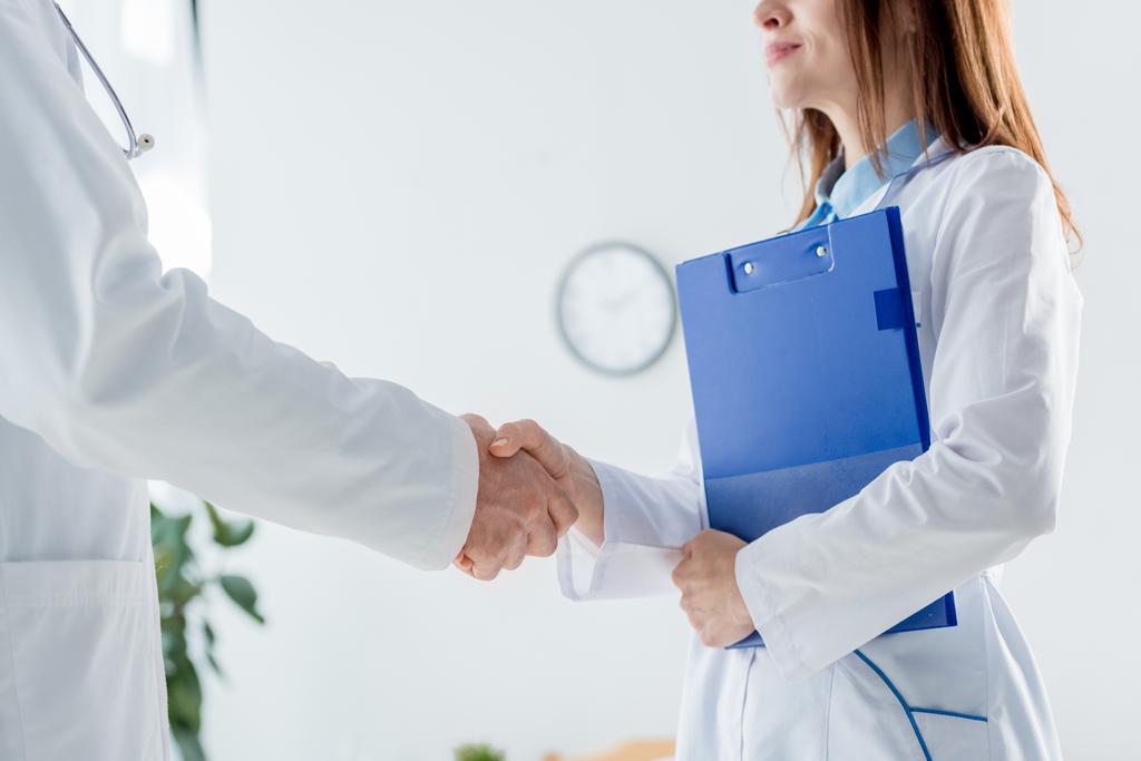 καλλιεργημένη άποψη του γιατρού με λευκό παλτό και ο συνάδελφός του σφίγγει το χέρι στο νοσοκομείο  - Φωτογραφία, εικόνα