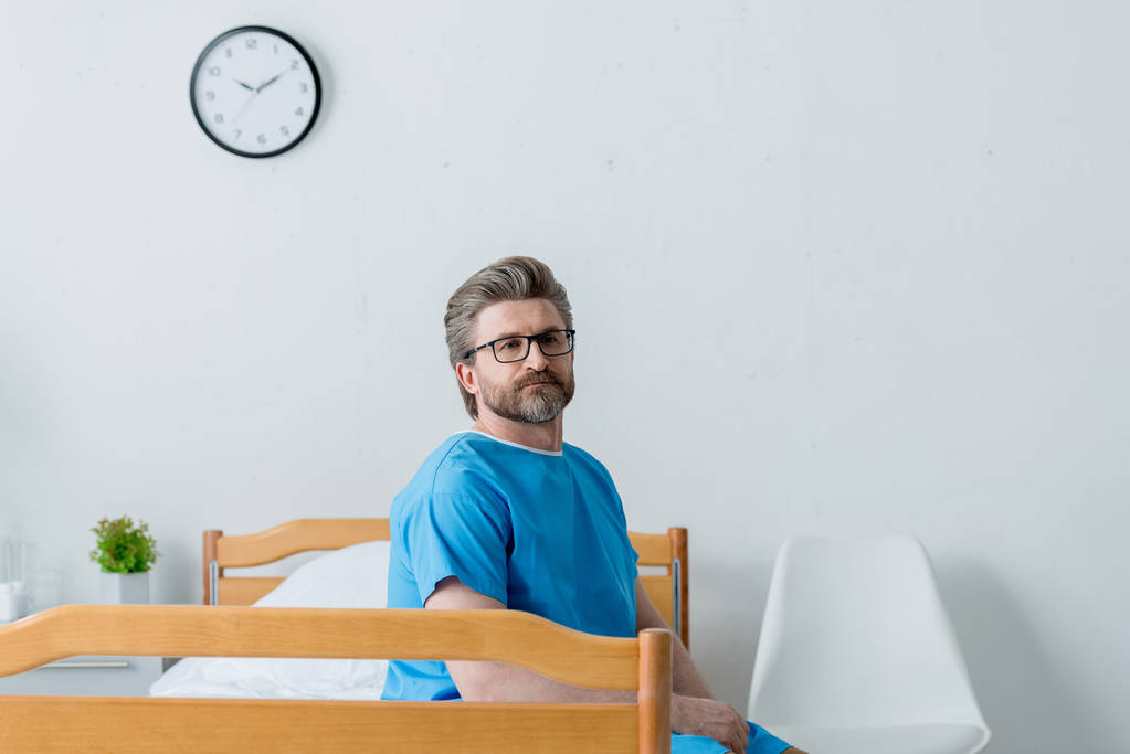 Patient im Arztkittel sitzt im Krankenhaus auf Bett  - Foto, Bild