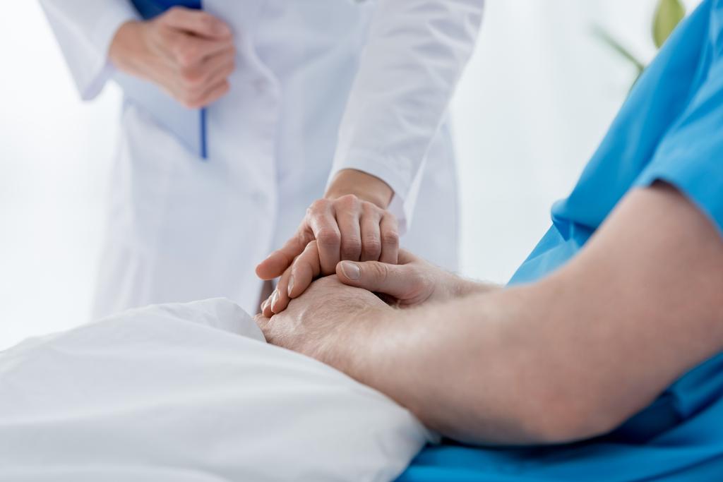 καλλιεργημένη άποψη του γιατρού σε λευκό παλτό κρατώντας το χέρι του ασθενούς στο νοσοκομείο  - Φωτογραφία, εικόνα