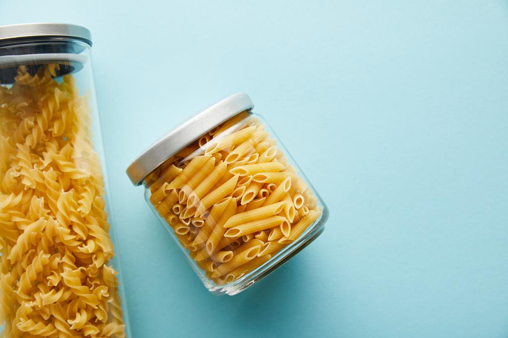 top view of raw penne and fusilli  in jars on blue background with copy space - Photo, Image