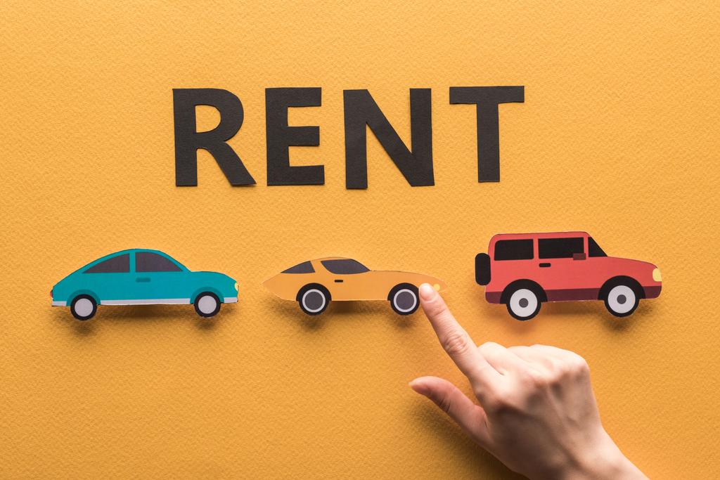 cropped view of woman pointing with finger at paper cut cars near rent lettering on orange background - Photo, Image