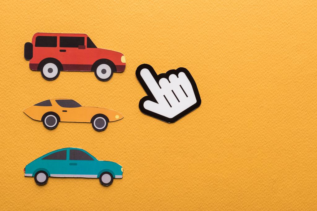 bovenaanzicht van papier gesneden auto 's, wijzende hand op oranje achtergrond - Foto, afbeelding