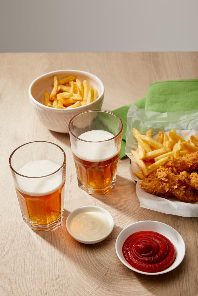 sklenice piva, kuřecí nugety s hranolky, kečup a majonéza na dřevěném stole na šedém pozadí - Fotografie, Obrázek