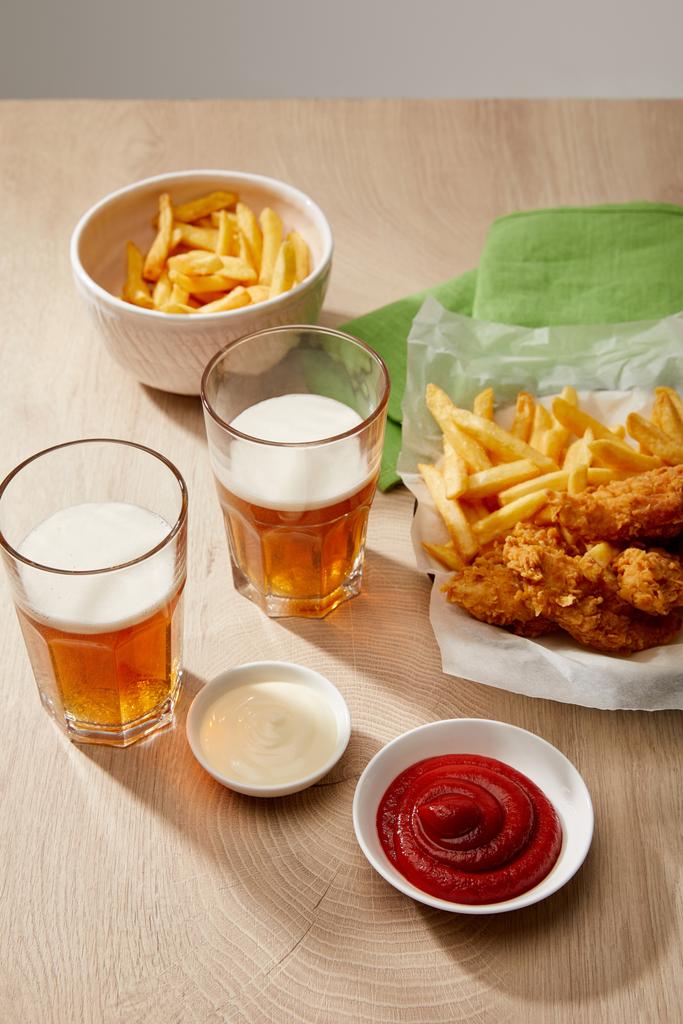 келихи пива, курячі нагетси з картоплею фрі, кетчупом та майонезом на дерев'яному столі на сірому фоні
 - Фото, зображення
