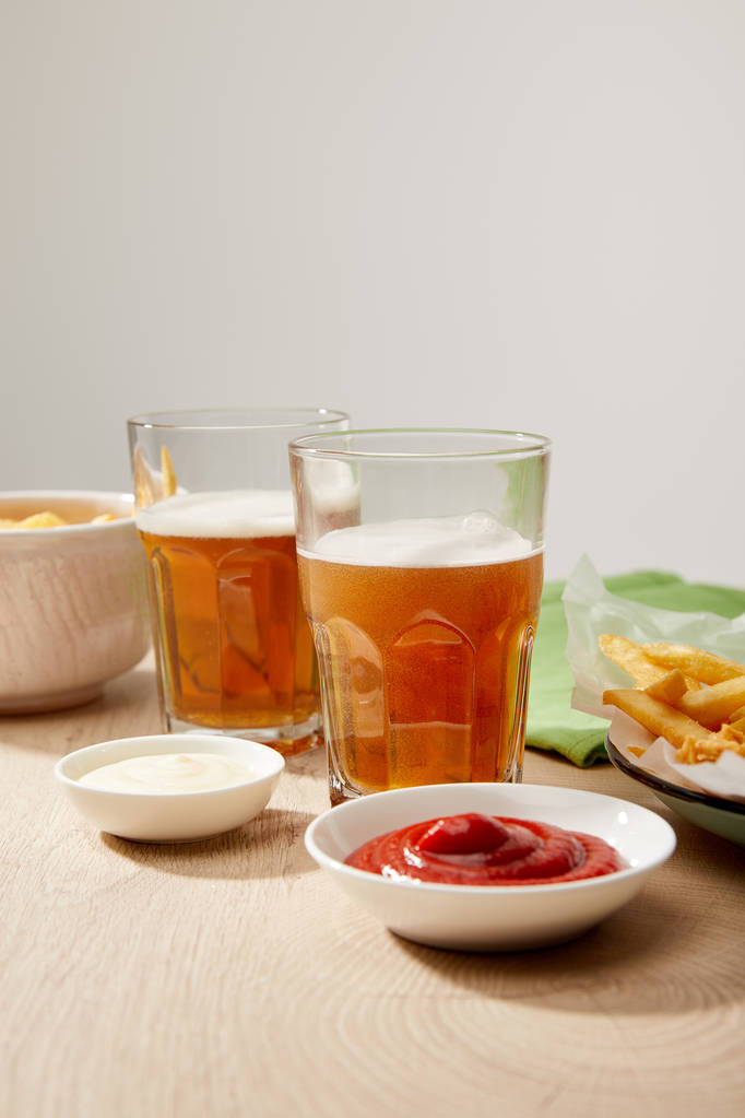 Bir bardak bira, patates kızartmalı tavuk nugget ketçap ve mayonez tahta masa üzerinde gri arka planda. - Fotoğraf, Görsel