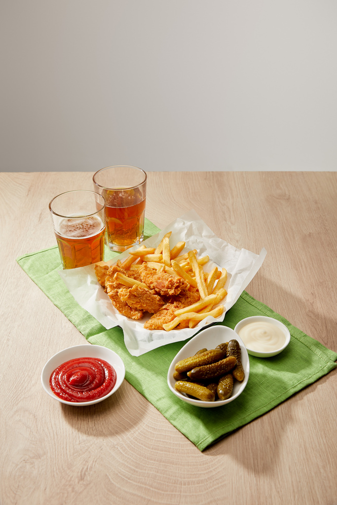 vasos de cerveza, pepitas de pollo con papas fritas, salsas y pepinillos sobre mesa de madera sobre fondo gris
 - Foto, imagen