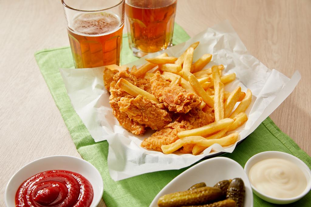 szklanki piwa, bryłki kurczaka z frytkami, sosami i korniszonami na drewnianym stole - Zdjęcie, obraz