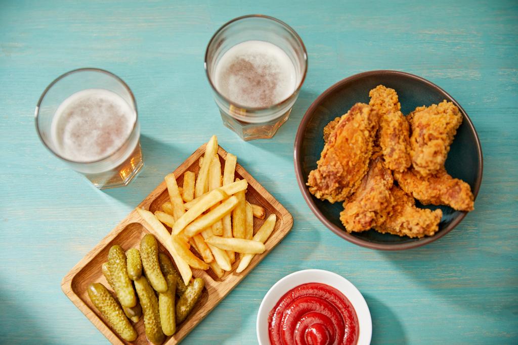 bovenaanzicht van heerlijke kipnuggets, ketchup, frietjes en augurken bij een glas bier op turquoise houten tafel - Foto, afbeelding