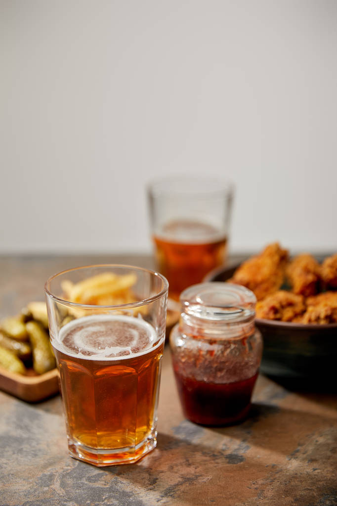 селективный фокус куриных наггетсов, картошки фри и огурцов возле бокалов пива на каменной поверхности, изолированных на серой
 - Фото, изображение