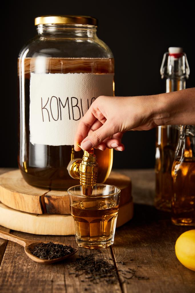 cropped view of woman pouring kombucha in glass from jar on wooden table isolated on black - Photo, Image