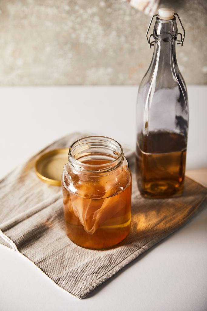 Kombu çaylı kavanoz şişenin yanında beyaz masadaki gri peçetenin üzerinde - Fotoğraf, Görsel