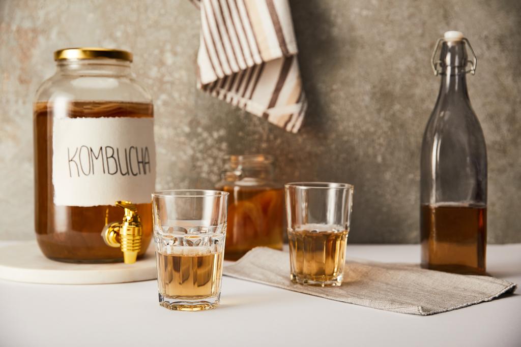 グラスの近くにコームブチャとストライプのナプキンと質感のグレーの背景にボトル入りジャー - 写真・画像