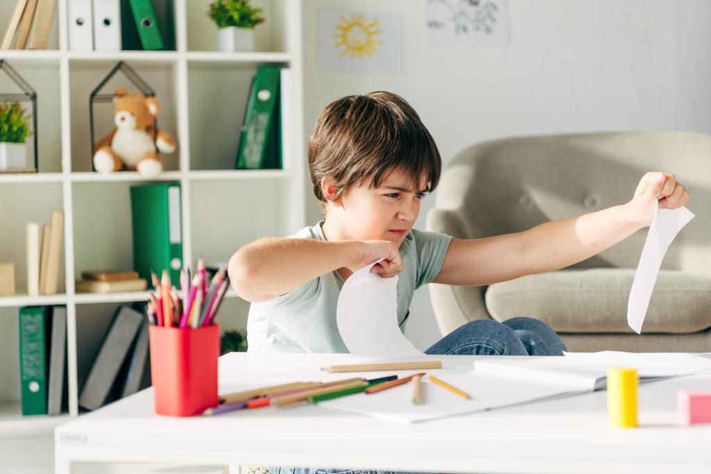 роздратована дитина з дислексією пробиває папір і сидить за столом
 - Фото, зображення