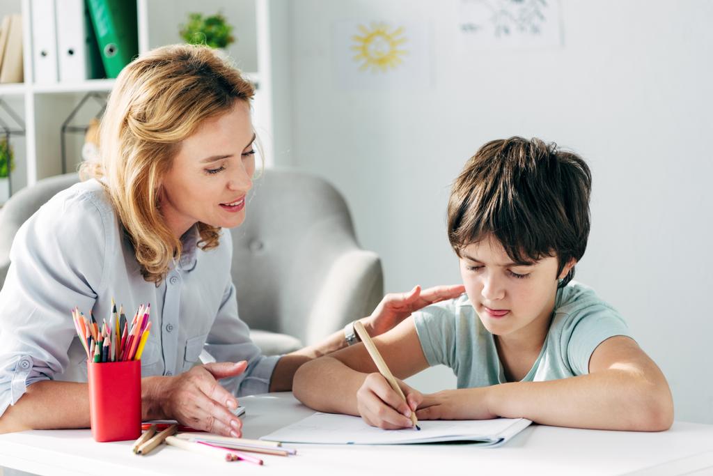 παιδί με δυσλεξία σχέδιο με μολύβι και παιδοψυχολόγος κοιτάζοντας το  - Φωτογραφία, εικόνα