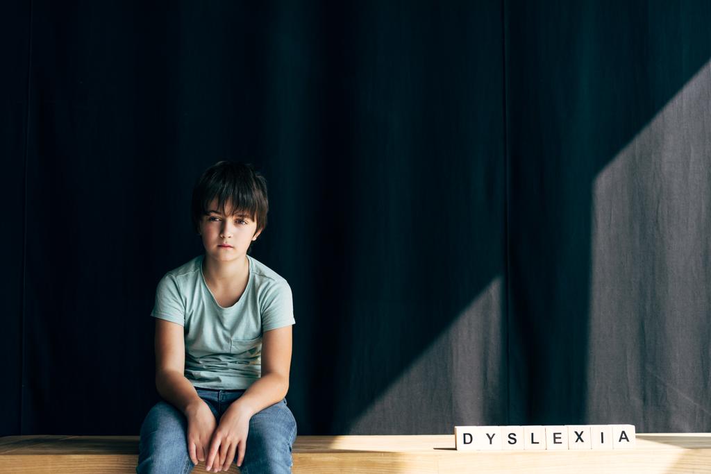 bambino con dislessia guardando la macchina fotografica e seduto vicino a cubi di legno con dislessia lettering
 - Foto, immagini