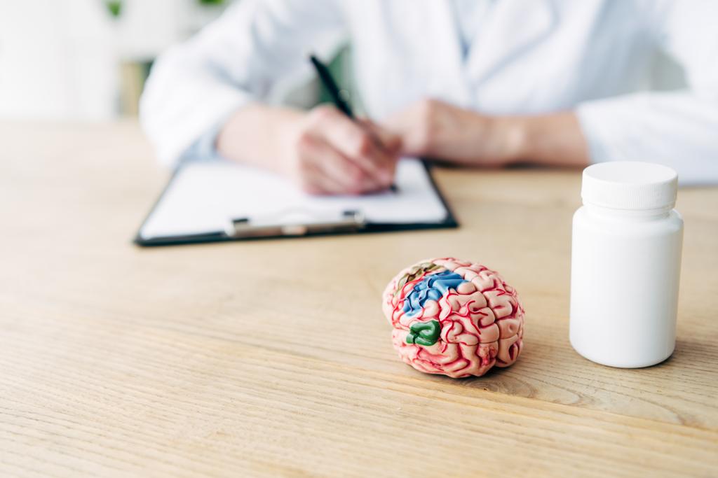 επιλεκτική εστίαση της φιάλης με χάπια και το μοντέλο του εγκεφάλου σε ξύλινο τραπέζι  - Φωτογραφία, εικόνα