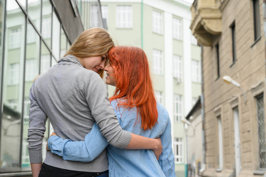 Związki tej samej płci. Szczęśliwa para lesbijek chodził wzdłuż ulicy i delikatnie przytulić się wokół talii. Grzbiety dwóch pięknych kobiet na randkę z bukietem z suszonych kwiatów. Lgbt. - Zdjęcie, obraz