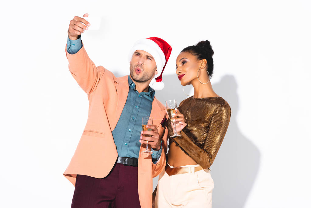Emotionaler Mann mit Weihnachtsmann spricht Selfie mit fröhlichem afrikanisch-amerikanischem Mädchen auf Weiß  - Foto, Bild