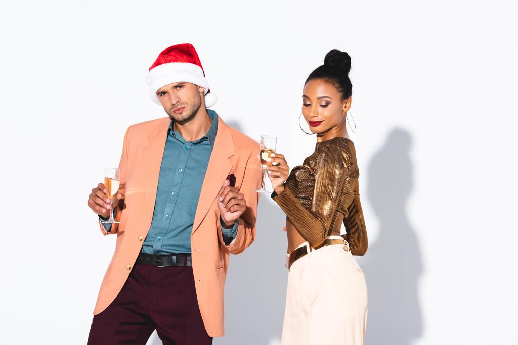 belle fille afro-américaine tenant verre de champagne près de l'homme en chapeau de Père Noël sur blanc
  - Photo, image