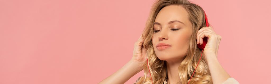 Blondynka z zamkniętymi oczami w słuchawce odizolowana na różowym ujęciu panoramicznym - Zdjęcie, obraz