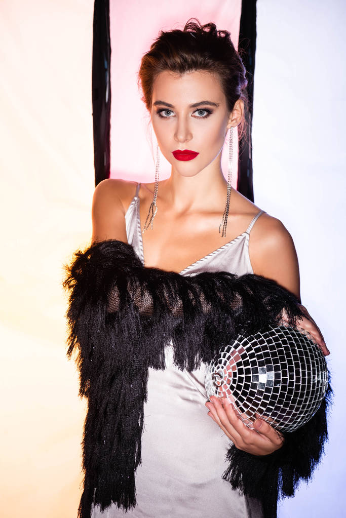 stylowa kobieta trzyma błyszczącą kulę disco na białym z czarnymi paskami - Zdjęcie, obraz