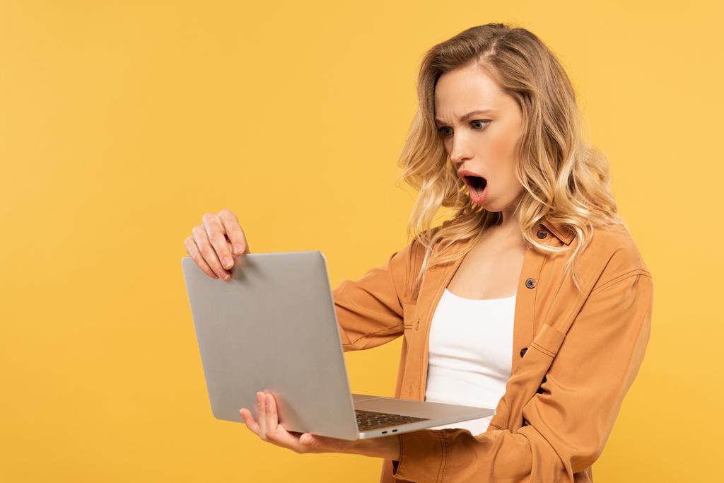 Scioccato donna bionda guardando il computer portatile isolato su giallo
 - Foto, immagini