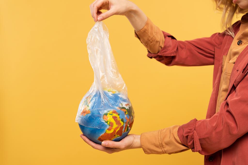 Widok kobiety trzymającej globus i plastikowe opakowanie odizolowane od żółtego, globalnego ocieplenia - Zdjęcie, obraz
