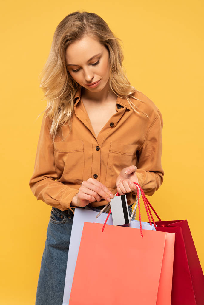 Blondine vrouw zet credit card in boodschappentas geïsoleerd op geel - Foto, afbeelding