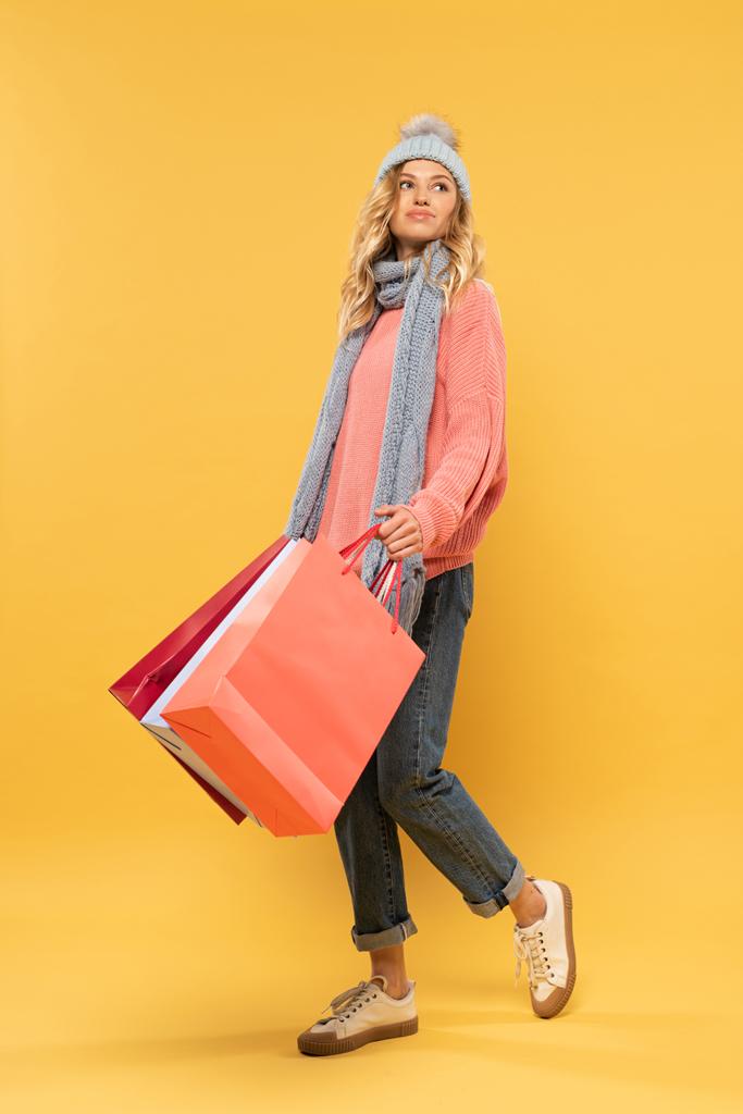 Woman in hat and scarf holding shopping bags on yellow background - 写真・画像