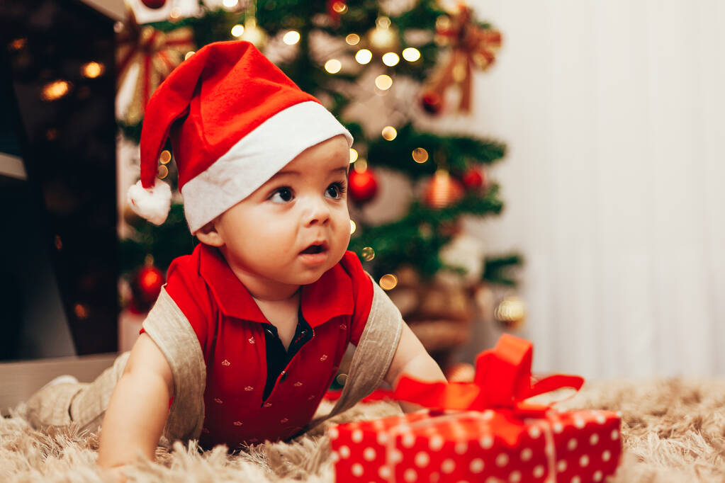 Baba játszik ajándék doboz a nappaliban padló felett karácsonyfa fények a háttérben - Fotó, kép