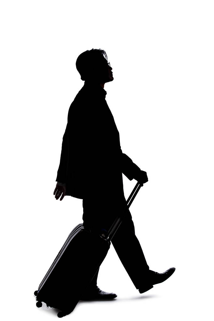 Σιλουέτα ενός επιχειρηματία που πηγαίνει σε ένα επαγγελματικό ταξίδι και ταξιδεύει με αποσκευές. Ο άνθρωπος κουβαλάει σακούλες σαν να ετοιμάζεται να επιβιβαστεί σε ένα αεροδρόμιο..  - Φωτογραφία, εικόνα
